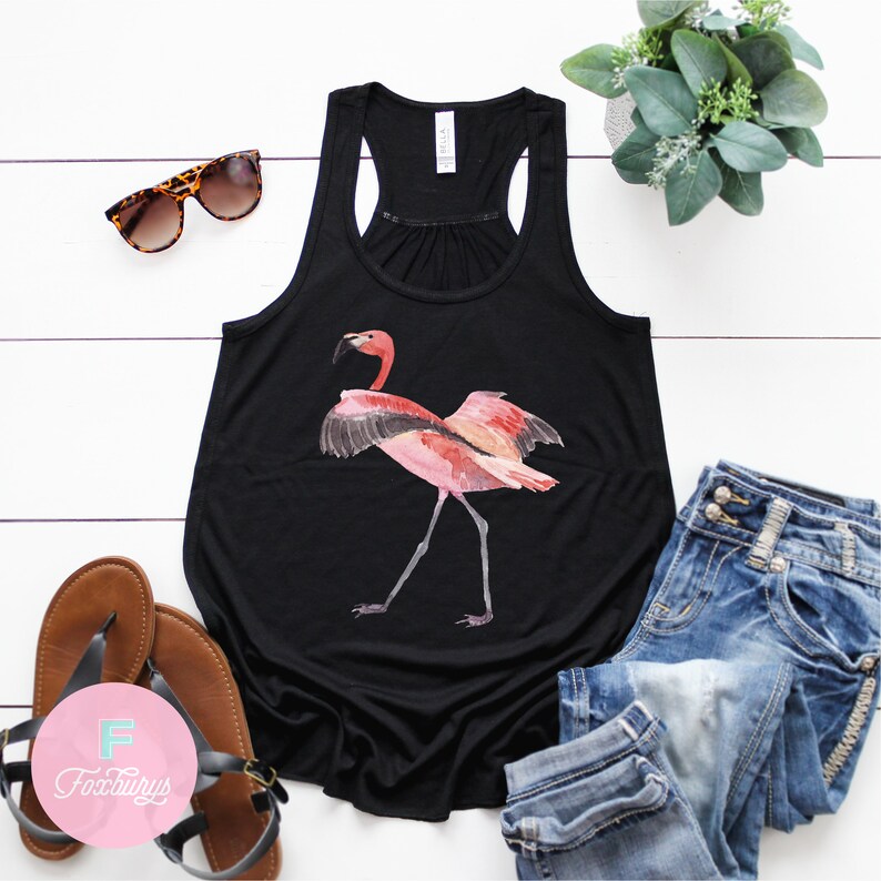 May include: Black tank top with a pink flamingo graphic. The flamingo is standing on one leg with its wings spread out. The tank top is a relaxed fit and has a scoop neck.