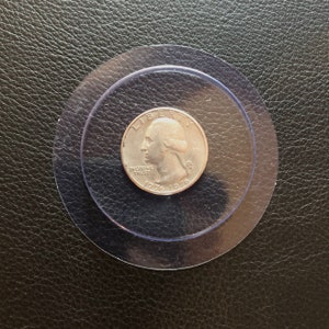 May include: A silver US quarter dollar coin with the image of George Washington on the obverse side. The coin is dated 1776-1976 and has the words "IN GOD WE TRUST" and "LIBERTY" inscribed on it.