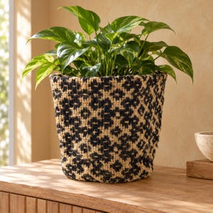 May include: A woven plant basket featuring a tan and black leopard print pattern. The cylindrical basket is constructed from a textured, natural fibre material and contains a lush green pothos plant with variegated heart-shaped leaves.