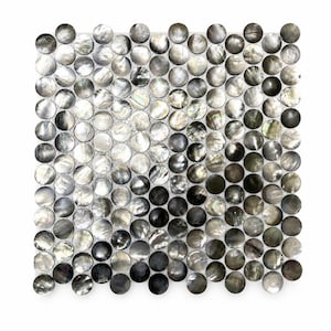 May include: Square mosaic tile made up of many small, round, iridescent tiles in grey, black, and white. The tiles have a pearlescent sheen, creating a shimmering effect. The mosaic is set against a white background.