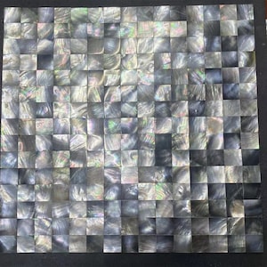 Op de afbeelding: Een vel met zwarte, iriserende mozaïektegels. Elke tegel is een vierkant met een licht afwijkend patroon van iriserende kleuren.