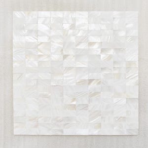 May include: Square mosaic tile composed of numerous small, rectangular, iridescent white pieces. The tiles have a subtle, pearlescent sheen, creating a textured, shimmering surface. The mosaic is set against a neutral, light-colored background.
