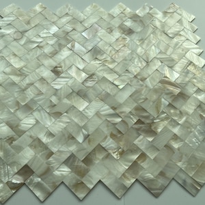 Può includere: Mosaico di piastrelle in madreperla bianca con un motivo a spina di pesce. Le piastrelle sono piccole e hanno una lucentezza naturale e iridescente.