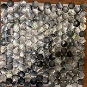 May include: A sheet of black and iridescent mother of pearl tile, arranged in a circular pattern. The tiles are approximately 1 inch in diameter.