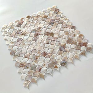 Op de afbeelding: Een vel met iriserende witte en beige mozaïektegels in een visgraatpatroon.