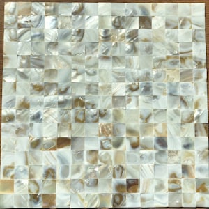 Puede incluir: Una lámina de azulejos de nácar iridiscente blanco y dorado. Cada azulejo es un cuadrado y mide aproximadamente 2,5 cm por 2,5 cm. Los azulejos están dispuestos en un patrón de cuadrícula.