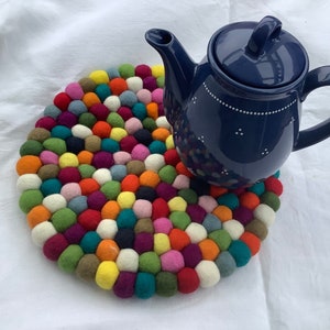 Könnte beinhalten: Eine blaue Keramik-Teekanne mit weißen Punkten steht auf einem bunten Filzuntersetzer aus vielen kleinen Kugeln.