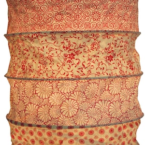 Könnte beinhalten: Zylindrischer Lampenschirm mit rotem und cremefarbenem Blumenmuster. Der Schirm besteht aus Stoff und hat ein mehrschichtiges Design mit einer Reihe horizontaler Bänder. Das obere Band hat ein geometrisches Design, die anderen florale und kreisförmige Muster.