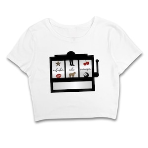 May include: White crop top featuring a black slot machine graphic. The slot machine displays a star, a high-heeled boot, and cherries. The words "alpha", "chi", and "omega" are also visible.
