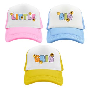 May include: Three trucker hats with a white front panel and a mesh back panel. The hats are pink, blue, and yellow. The front panel of each hat has a different word written in colorful letters with smiley faces. The pink hat says "LITTLE", the blue hat says "BIG", and the yellow hat says "GBIG".