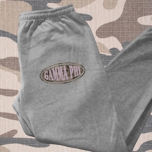 May include: Gray sweatpants with a camo print oval patch that says "GAMMA PHI" in pink letters.