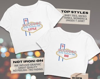 Könnte beinhalten: Zwei weiße T-Shirts mit einer Grafik eines Schildes mit der Aufschrift "Welcome to the Fabulous Fam". Eines der Shirts trägt die Aufschrift "Little" und das andere "Big". Die Shirts haben ein Retro-Design mit blauen, roten und goldenen Akzenten.