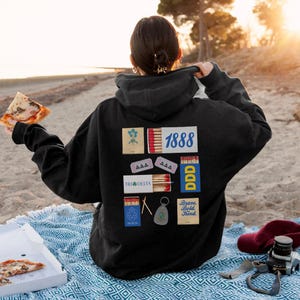 May include: Black hooded sweatshirt with a variety of colorful patches and text, including "1888", "Tri Delta", "Brave, Bold, Kind", and "AAA".