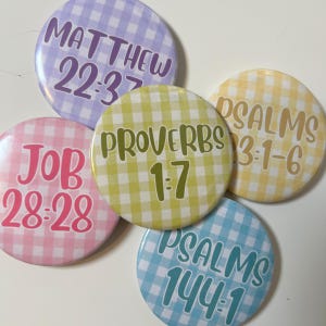 May include: Five circular pin-back buttons featuring a gingham check pattern in pastel colors. Each button displays a Bible verse reference: Matthew 22:37 in purple, Proverbs 1:7 in green, Psalms 3:1-6 in yellow, Job 28:28 in pink, and Psalms 144:1 in blue.