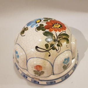 Könnte beinhalten: Eine weiße Keramikkuppel mit einem Blumendesign. Die Kuppel hat ein blaues, rotes und grünes Blumenmuster auf weißem Hintergrund. Die Kuppel hat einen gewellten Rand.