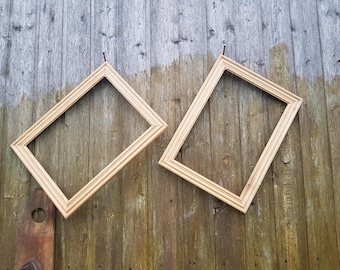 May include: Two empty, light-colored wooden picture frames are mounted on a weathered wooden wall. The frames are rectangular with a beveled edge, and are angled slightly. The wood grain of the wall is visible.