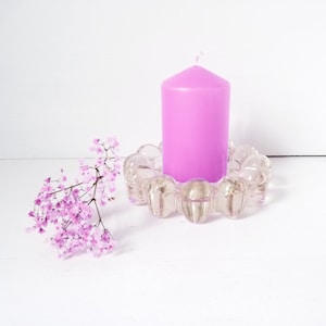 May include: A clear glass candle holder with a textured design holds a single pink candle.