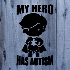 May include: Black and white graphic design on a wood background. The design features a superhero silhouette with a puzzle piece on their chest and the text "My Hero Has Autism".