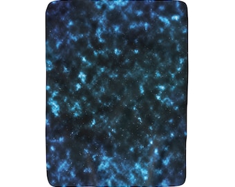 Puede incluir: Una manta de color azul oscuro y negro con temática de galaxia con un patrón de nebulosa en espiral y estrellas blancas dispersas.