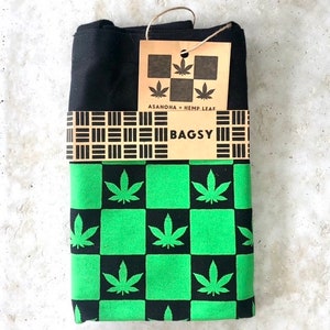 May include: Black and green checkered fabric with a hemp leaf pattern. The fabric is folded and has a brown tag with the text "ASANOHA + HEMP LEAF" and "BAGSY".