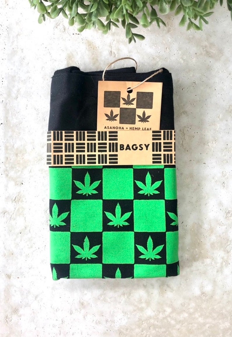 May include: Black and green checkered fabric with a hemp leaf pattern. The fabric is folded and has a brown tag with the text "ASANOHA + HEMP LEAF" and "BAGSY".