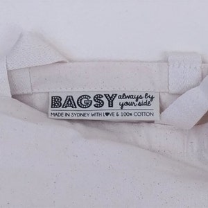 May include: White canvas tote bag with a black label that reads "BAGSY always by your side" and "MADE IN SYDNEY WITH LOVE & 100% COTTON".