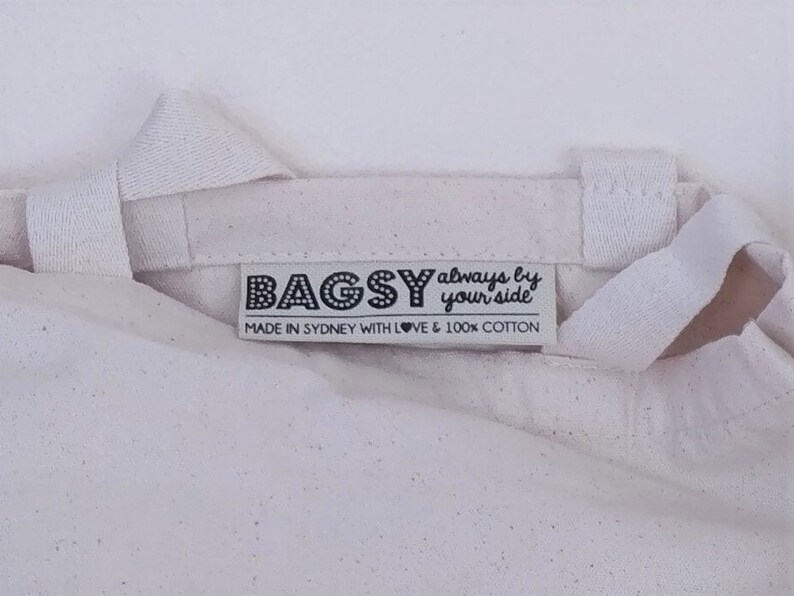 May include: White canvas tote bag with a black label that reads "BAGSY always by your side" and "MADE IN SYDNEY WITH LOVE & 100% COTTON".