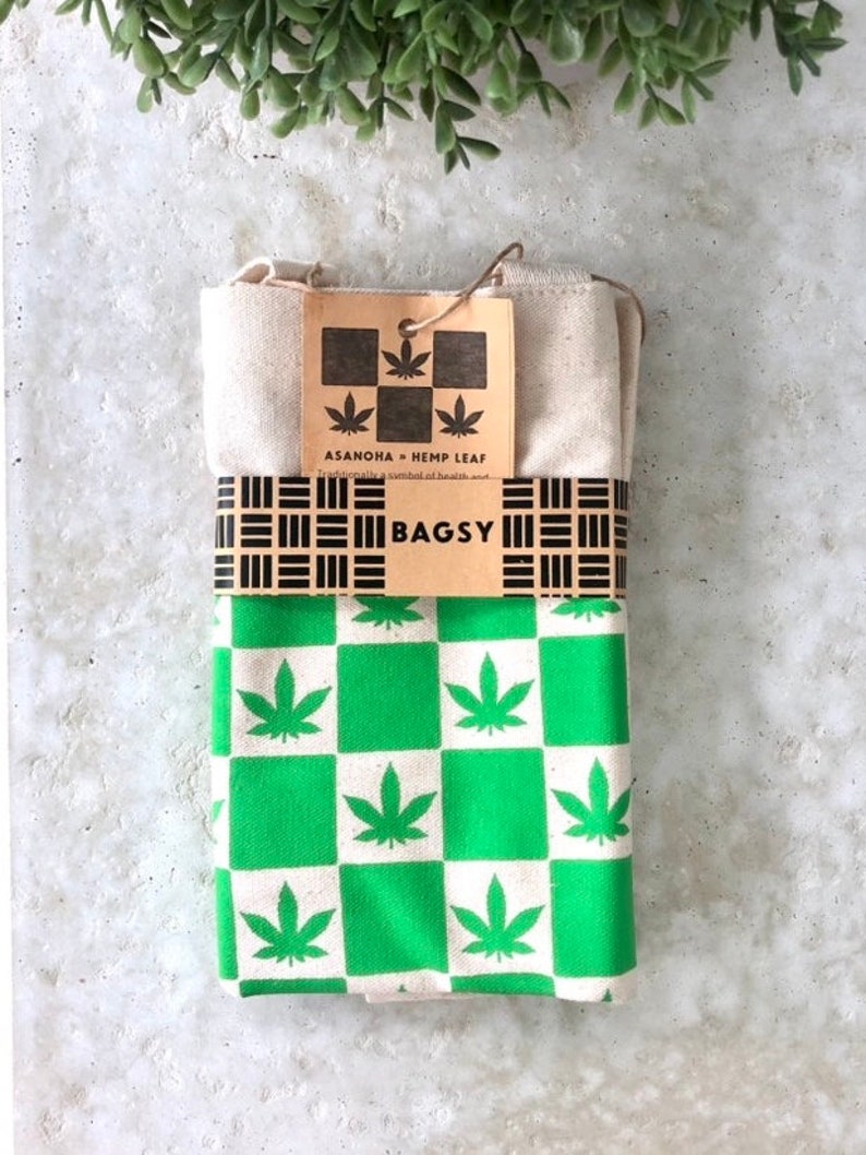 May include: A green and white checkered tote bag with a hemp leaf design. The bag is folded and has a brown tag that reads "ASANOHIA - HEMP LEAF" and "BAGSY".