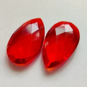 Puede incluir: Dos cuentas de vidrio rojas facetadas en forma de lágrima.