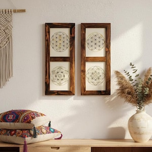 Könnte beinhalten: Zwei vertikale, rechteckige Wandrahmen aus dunkelbraunem Holz, die jeweils zwei cremefarbene Paneele mit schwarzen und goldenen geometrischen Linienmustern enthalten. Die Designs zeigen komplexe kreisförmige Motive der heiligen Geometrie.