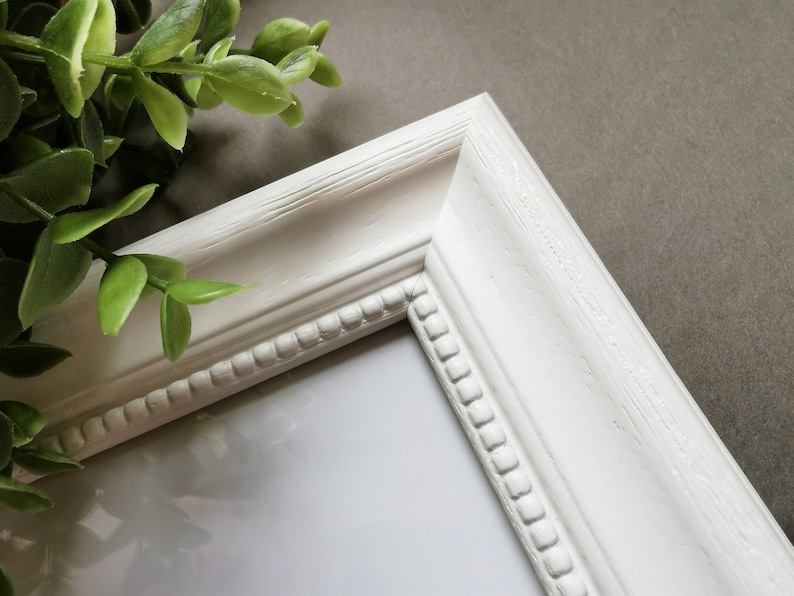 May include: White picture frame with a decorative beaded edge. The frame is made of wood and has a smooth, matte finish.