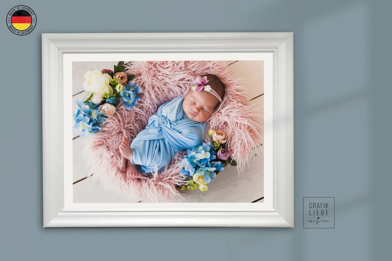 May include: A newborn baby wrapped in a blue blanket is sleeping on a pink fluffy surface surrounded by flowers. The baby is wearing a white headband with a pink flower.