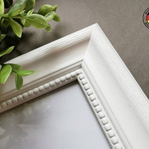 May include: White picture frame with a beaded edge and a white mat. The frame is made in Germany.