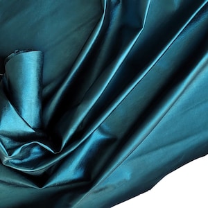Puede incluir: Tela de satén de color turquesa con una textura suave y sedosa. La tela está drapeada y doblada, creando pliegues y curvas suaves.