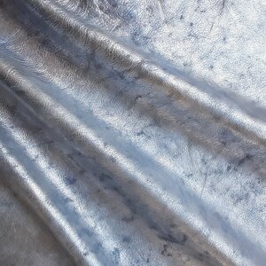 Pu&ograve; includere: Primo piano di un tessuto in pelle argentata con una superficie testurizzata e un aspetto stropicciato.