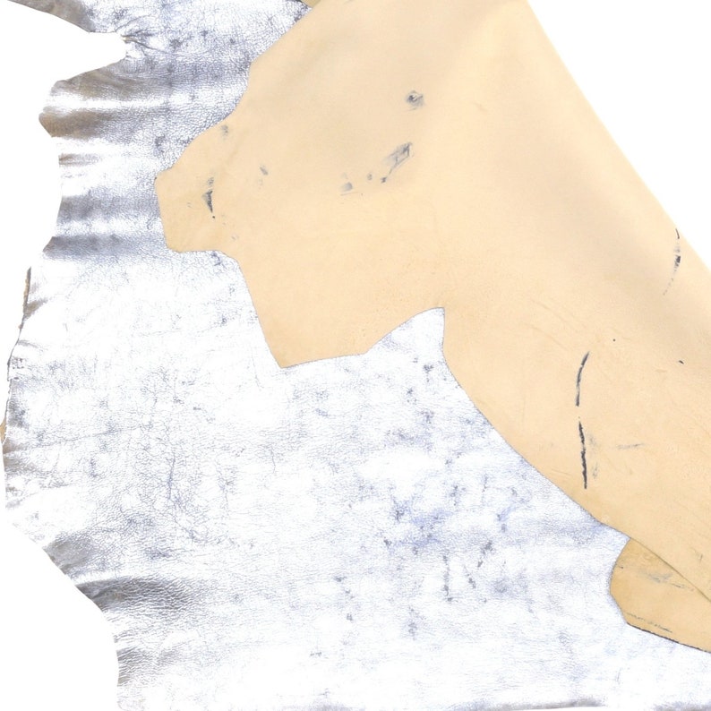 Pu&ograve; includere: Un pezzo di pelle argentata con una toppa di pelle beige in cima. La pelle argentata ha una superficie testurizzata.