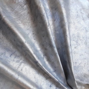 Pu&ograve; includere: Primo piano di un tessuto in pelle argentata con una texture grinzosa.