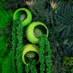 Puede incluir: Una vibrante obra de arte mural verde con tres recipientes esf&eacute;ricos abiertos llenos de vegetaci&oacute;n texturizada. Plantas verdes colgantes caen en cascada hacia abajo, complementadas por un fondo de varios follajes verdes, creando una est&eacute;tica natural exuberante.