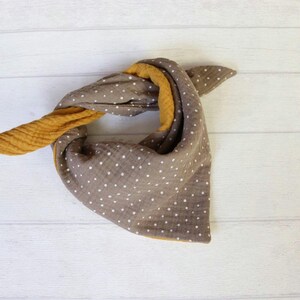 May include: A brown and yellow bandana-style scarf with white polka dots. The scarf is folded and tied, showcasing the contrasting colors and textures of the fabric. The scarf is made of soft, lightweight material.