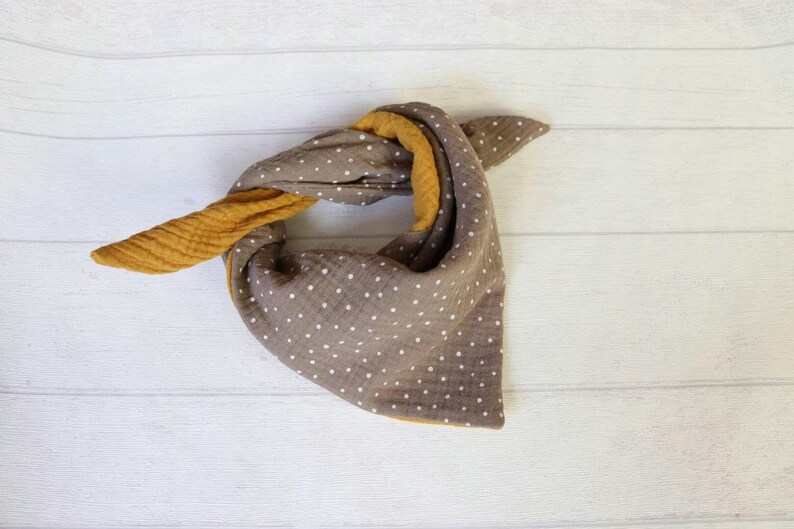 May include: A brown and yellow bandana-style scarf with white polka dots. The scarf is folded and tied, showcasing the contrasting colors and textures of the fabric. The scarf is made of soft, lightweight material.