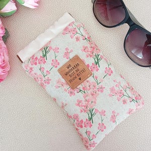 Könnte beinhalten: Ein rechteckiges Stoffetui mit beigefarbenem Grund, rosa Blumenmuster und weißem oberen Rand. Auf der Vorderseite befindet sich ein quadratischer brauner Lederaufnäher mit dem Text WIE WUNDERBAR BIST DU DENN BITTE! und einem kleinen Herz.