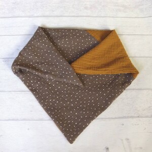 May include: A brown and mustard yellow baby bib. The bib is made of soft, textured fabric. The brown section has a white polka dot pattern. The bib is folded in a triangle shape.