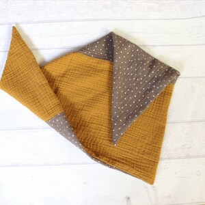 May include: Mustard yellow and brown baby blanket with a polka dot pattern. The blanket is made of a soft, textured fabric. The blanket is folded in a triangular shape, with the brown polka dot fabric visible on the edges.