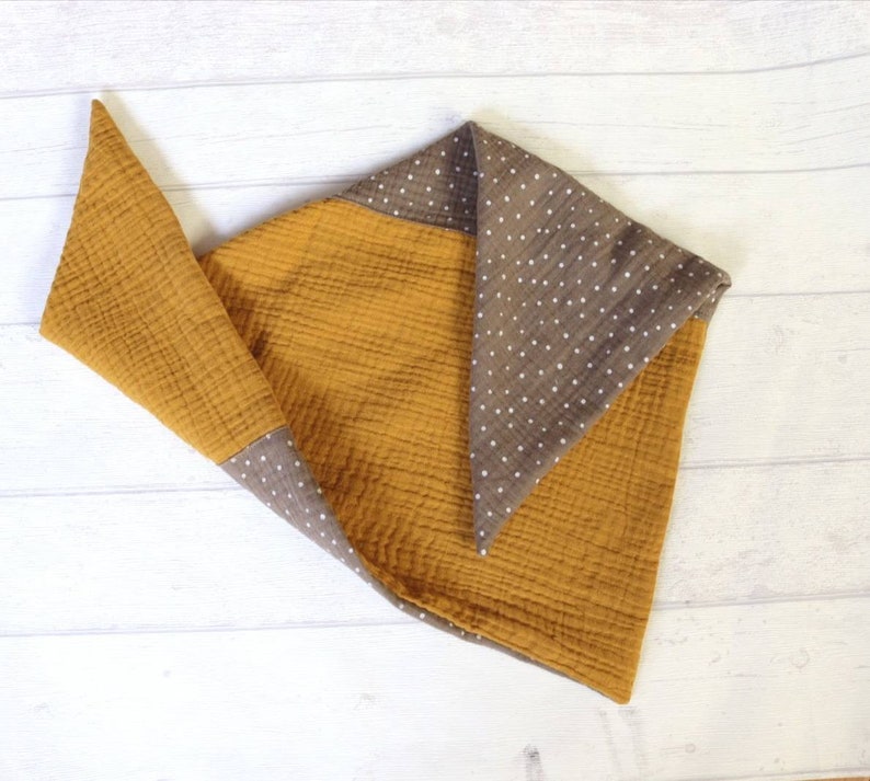 May include: Mustard yellow and brown baby blanket with a polka dot pattern. The blanket is made of a soft, textured fabric. The blanket is folded in a triangular shape, with the brown polka dot fabric visible on the edges.
