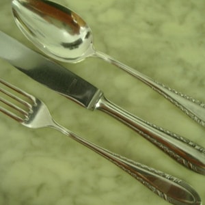 Könnte beinhalten: Ein Set aus drei versilberten Besteckteilen, bestehend aus einer Gabel, einem Messer und einem Löffel. Jedes Teil ist mit einem verzierten Design versehen.