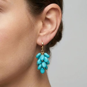 May include: Gold-tone hoop earrings with a cluster of turquoise-colored beads. The earrings have a small gold bead at the end of each turquoise bead. The earrings are a dangle style.