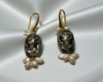 May include: A pair of gold-tone earrings featuring oval, gray and black pendants with a cameo design. The earrings have a cluster of small, white pearls at the bottom and top of the pendants.