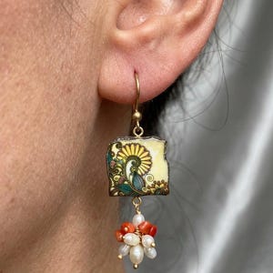 May include: Gold-tone dangle earrings. Each earring features a square, yellow and green floral tile design, with a cluster of orange coral and white pearls. The earrings are attached to a gold-tone ear wire.
