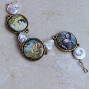 Puede incluir: Una pulsera dorada con pinturas en miniatura de arte clásico, incluyendo "El nacimiento de Venus" de Botticelli y la Mona Lisa. La pulsera está adornada con perlas irregulares e iridiscentes y un cierre de gancho.