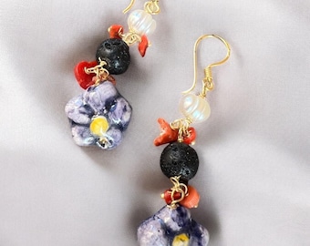 May include: Purple and yellow ceramic flower dangle earrings with red coral, black lava rock, and white pearl beads.